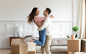 glückliches Paar umarmt sich im neuen Zuhause, umgeben von Umzugkartons