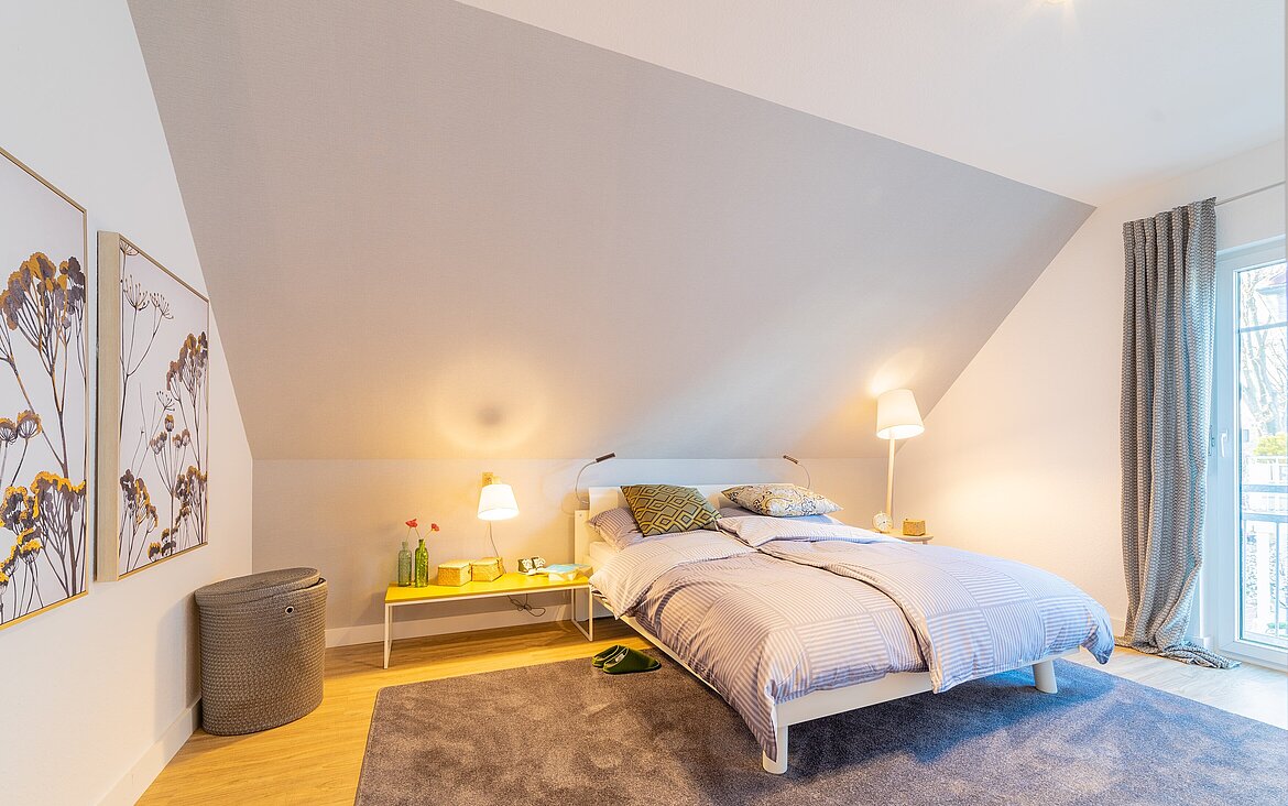 breites Bett mit Nachtschränken und warmer indirekter Beleuchtung unter einer Dachschräge