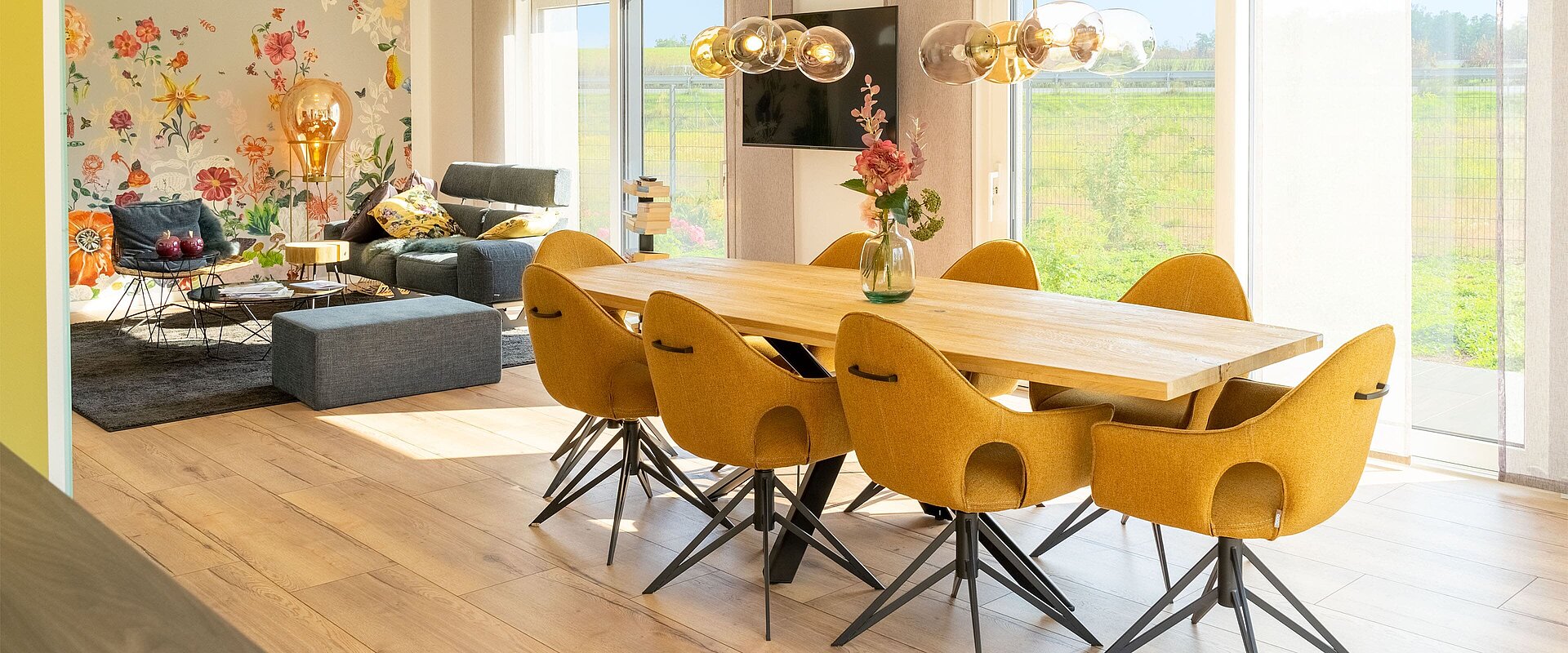 modernes Wohnzimmer mit Essebereich vor Fensterfront und Wohnlandschaft mit Blumenakzenttapete