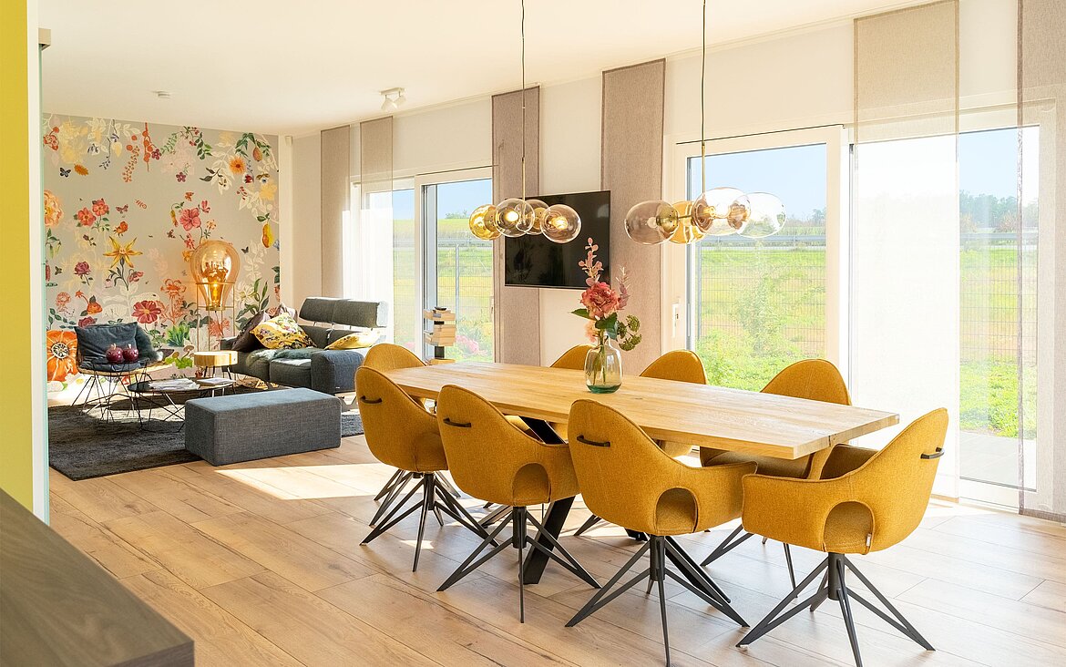 modernes Wohnzimmer mit Essebereich vor Fensterfront und Wohnlandschaft mit Blumenakzenttapete