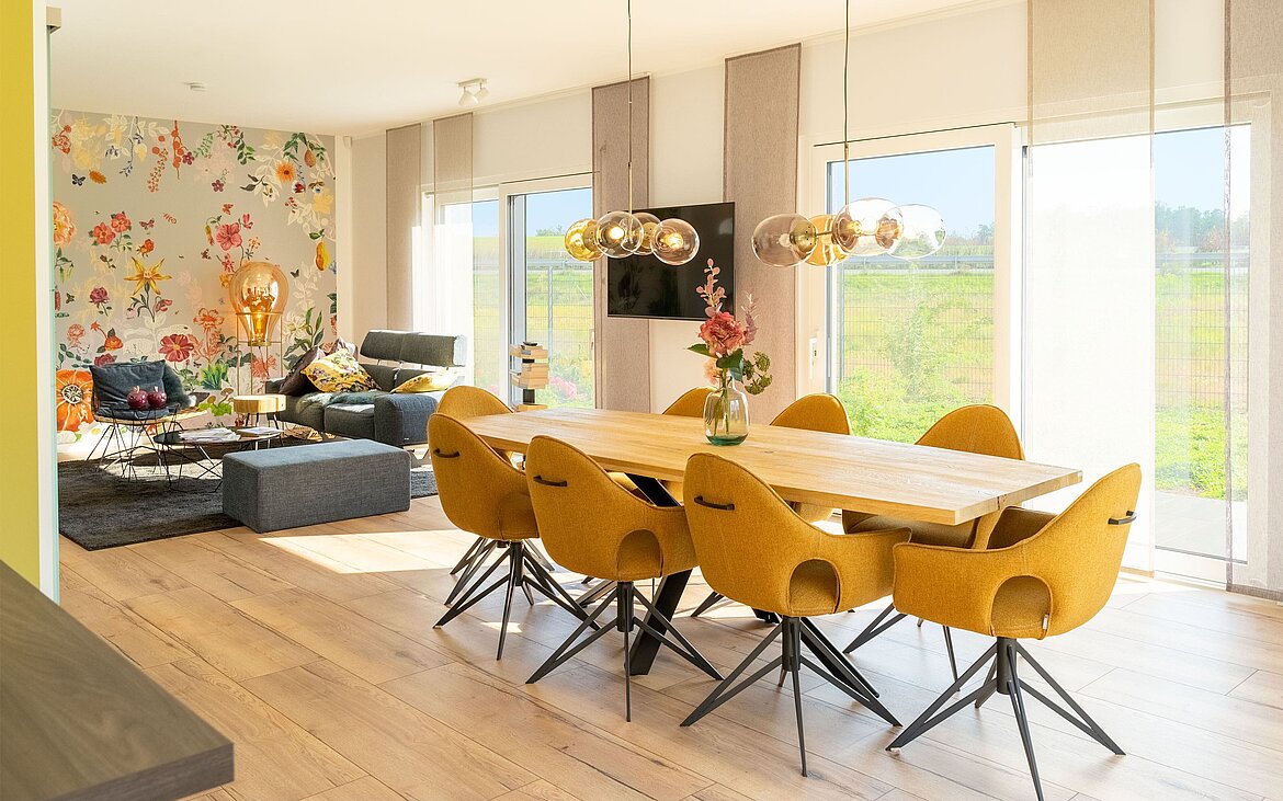modernes Wohnzimmer mit Essebereich vor Fensterfront und Wohnlandschaft mit Blumenakzenttapete