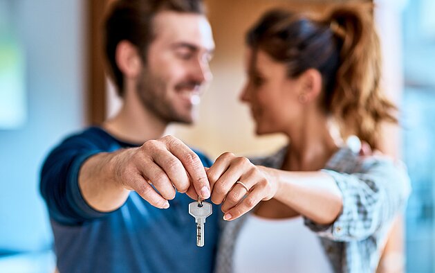 Pärchen schaut sich an und hält gemeinsam einen Haustürschlüssel vor sich